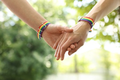 Photo of LGBT concept. Women in rainbow wristbands holding hands outdoors, closeup