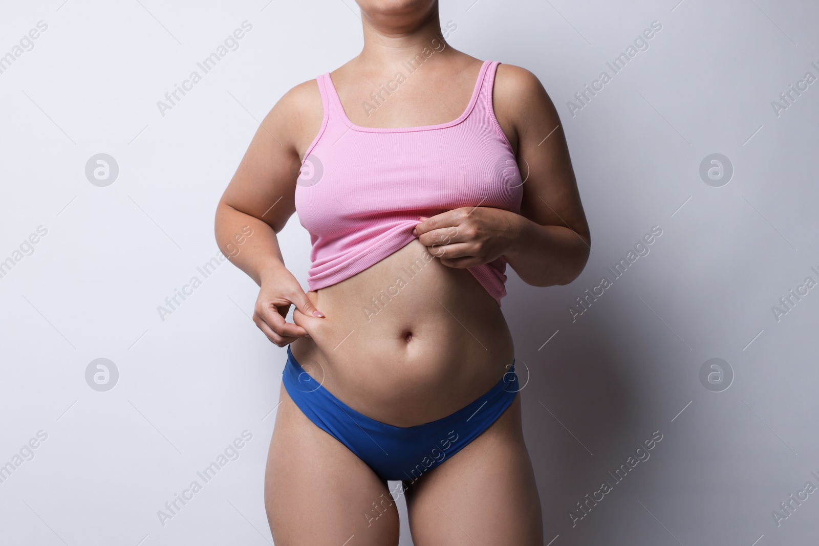 Photo of Liposuction. Woman in underwear touching her belly on light grey background, closeup