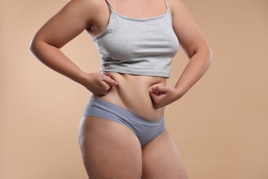 Photo of Liposuction. Woman in underwear touching her belly on beige background, closeup