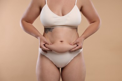Photo of Liposuction. Woman in underwear touching her belly on beige background, closeup