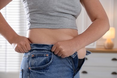 Photo of Liposuction. Woman trying to put on tight jeans at home, closeup