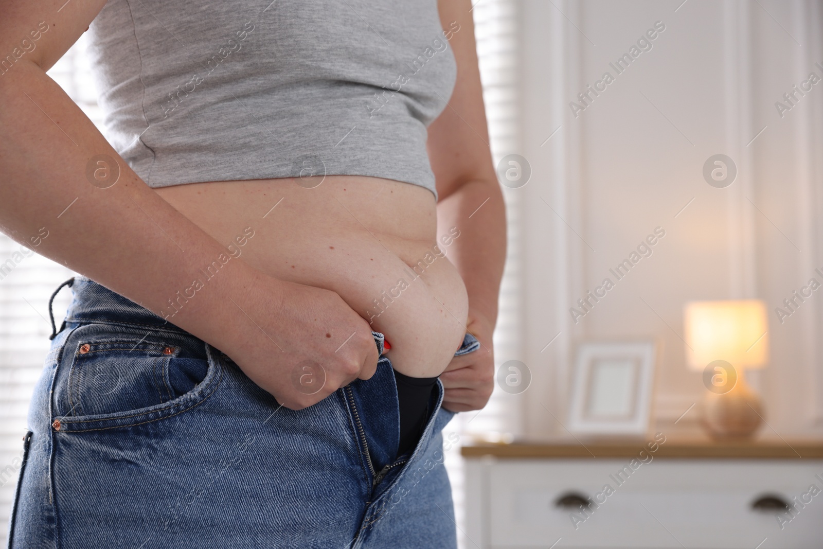 Liposuction. Woman trying to put on tight jeans at home, closeup. Space for text Photo of Liposuction. Woman trying to put on tight jeans at home, closeup. Space for text