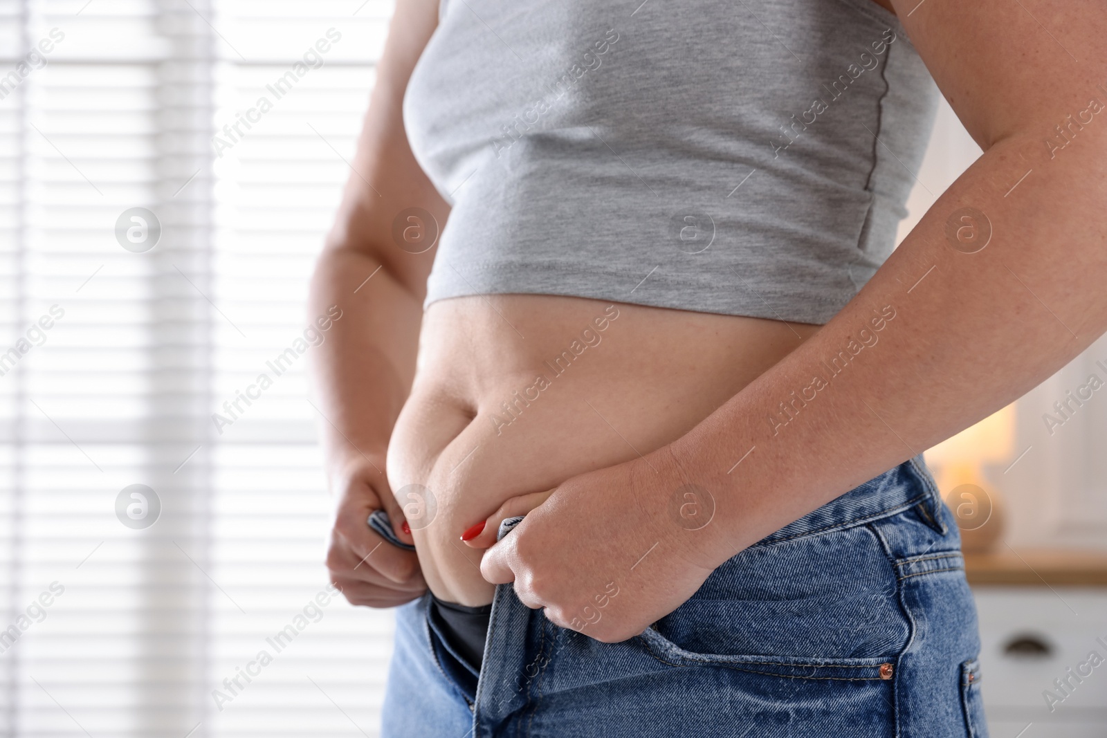 Liposuction. Woman trying to put on tight jeans at home, closeup Photo of Liposuction. Woman trying to put on tight jeans at home, closeup