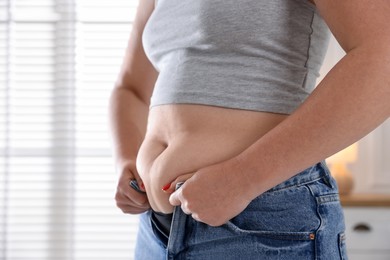 Photo of Liposuction. Woman trying to put on tight jeans at home, closeup