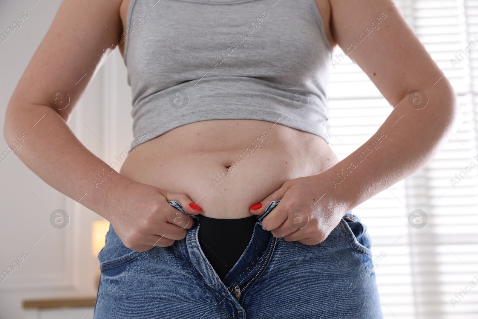 Liposuction. Woman trying to put on tight jeans at home, closeup Photo of Liposuction. Woman trying to put on tight jeans at home, closeup