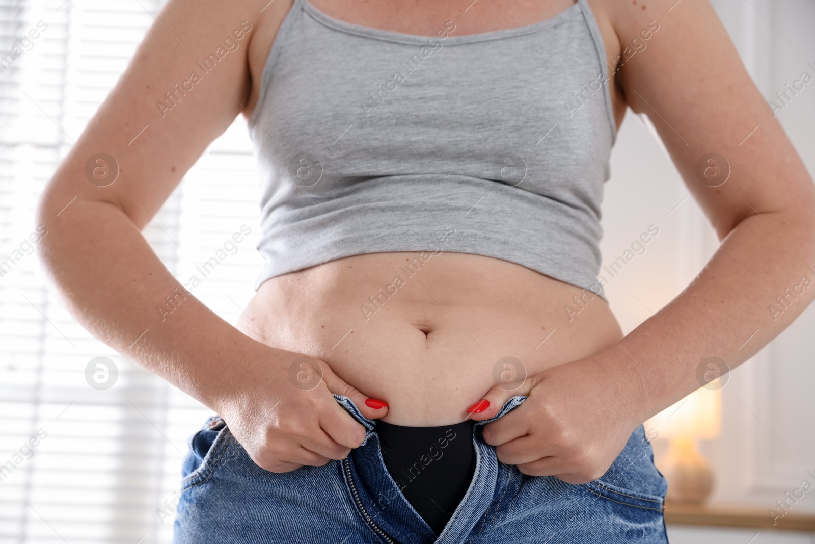 Liposuction. Woman trying to put on tight jeans at home, closeup Photo of Liposuction. Woman trying to put on tight jeans at home, closeup