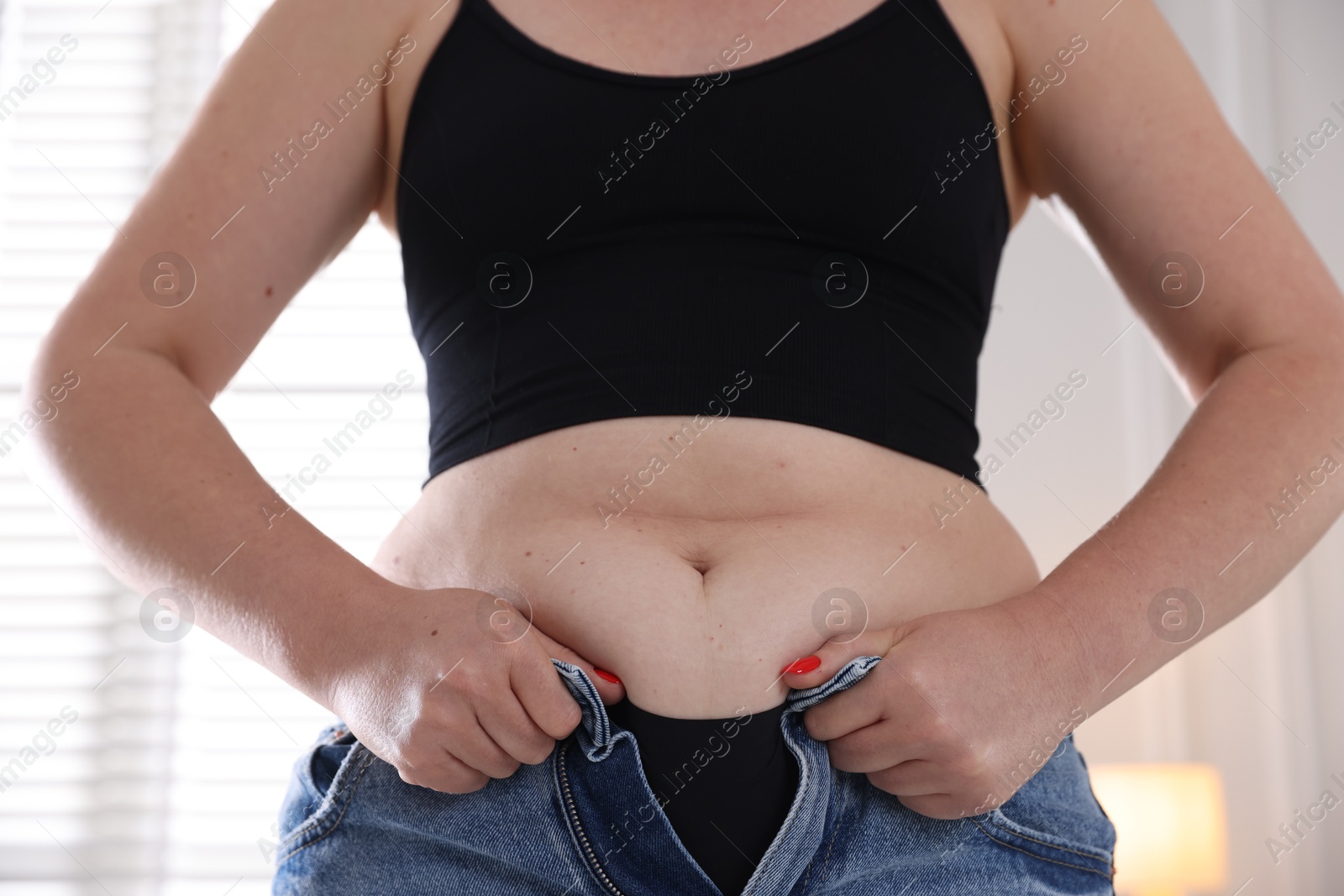 Liposuction. Woman trying to put on tight jeans at home, closeup Photo of Liposuction. Woman trying to put on tight jeans at home, closeup