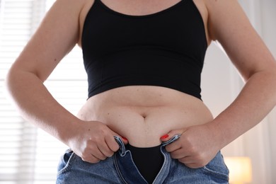 Photo of Liposuction. Woman trying to put on tight jeans at home, closeup