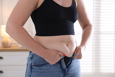 Photo of Liposuction. Woman trying to put on tight jeans at home, closeup