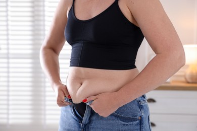 Photo of Liposuction. Woman trying to put on tight jeans at home, closeup