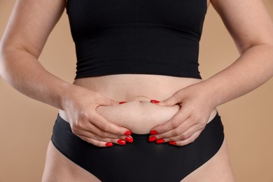 Photo of Liposuction. Woman in underwear touching her belly on beige background, closeup