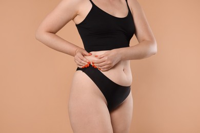 Photo of Liposuction. Woman in underwear touching her side on beige background, closeup