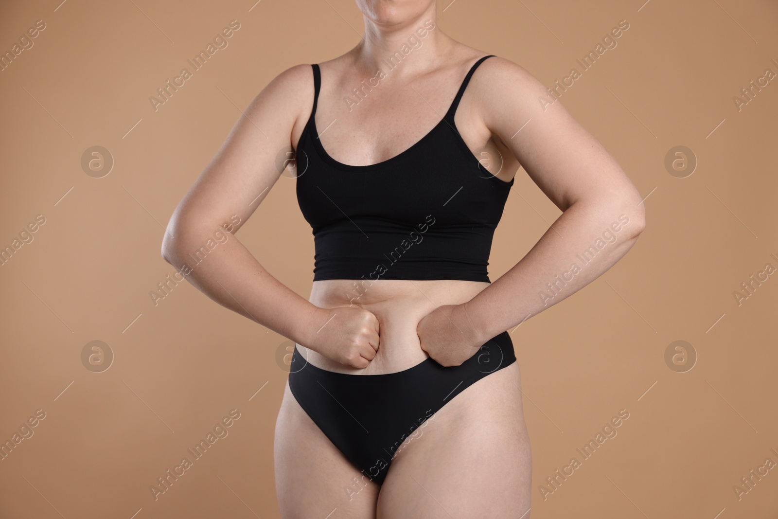 Photo of Liposuction. Woman in underwear touching her belly on beige background, closeup