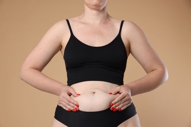 Photo of Liposuction. Woman in underwear touching her belly on beige background, closeup