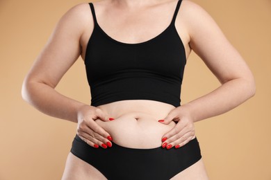 Photo of Liposuction. Woman in underwear touching her belly on beige background, closeup