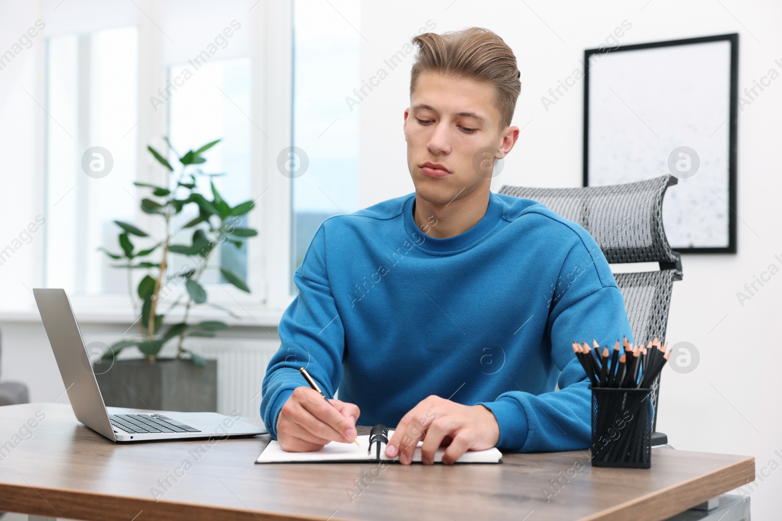 Copywriter with laptop writing in notebook at wooden table indoors Photo of Copywriter with laptop writing in notebook at wooden table indoors