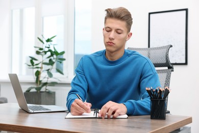 Photo of Copywriter with laptop writing in notebook at wooden table indoors