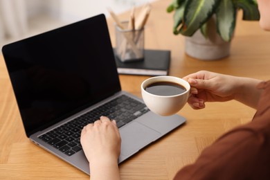 Photo of Copywriter with cup of drink using laptop at wooden table indoors, closeup