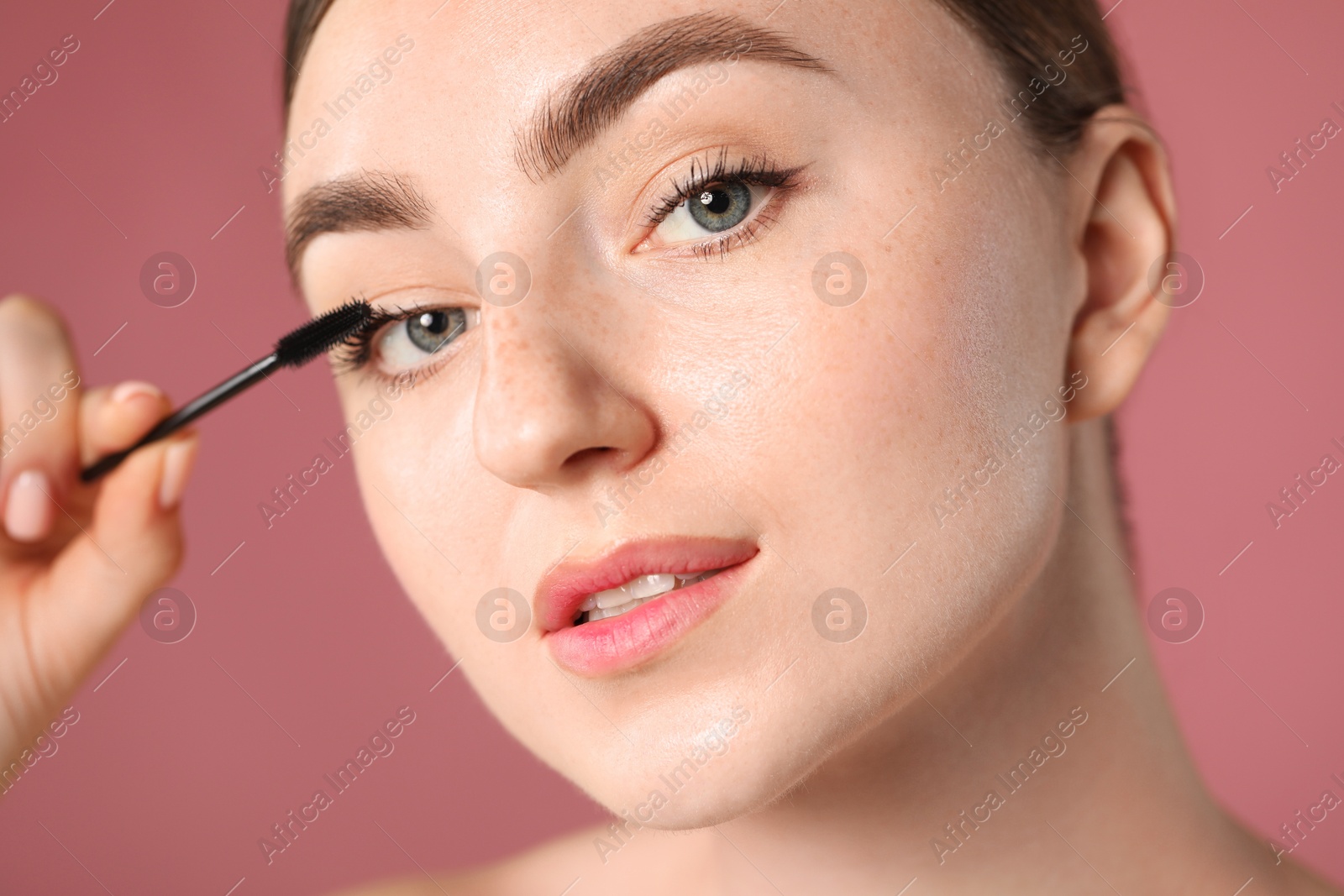 Young woman applying mascara onto her eyelashes on pink background, closeup Photo of Young woman applying mascara onto her eyelashes on pink background, closeup