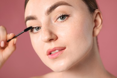 Photo of Young woman applying mascara onto her eyelashes on pink background, closeup
