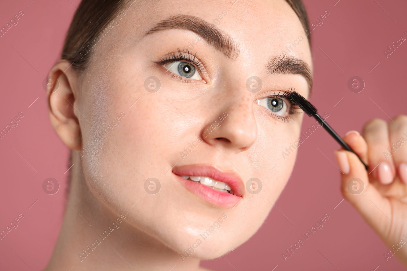 Young woman applying mascara onto her eyelashes on pink background, closeup Photo of Young woman applying mascara onto her eyelashes on pink background, closeup