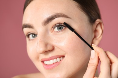 Photo of Young woman applying mascara onto her eyelashes on pink background, closeup