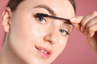 Photo of Young woman applying mascara onto her eyelashes on pink background, closeup