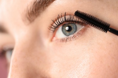 Photo of Young woman applying mascara onto her eyelashes, closeup