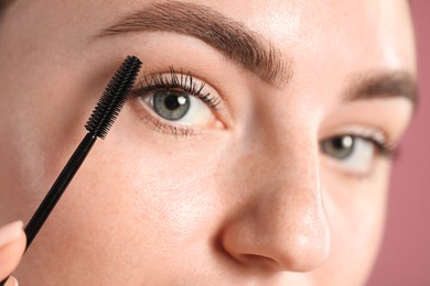 Photo of Young woman applying mascara onto her eyelashes on pink background, closeup