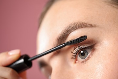 Photo of Young woman applying mascara onto her eyelashes on pink background, closeup