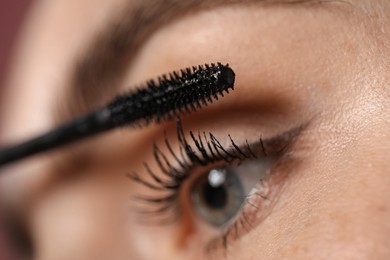 Photo of Young woman applying mascara onto her eyelashes, closeup