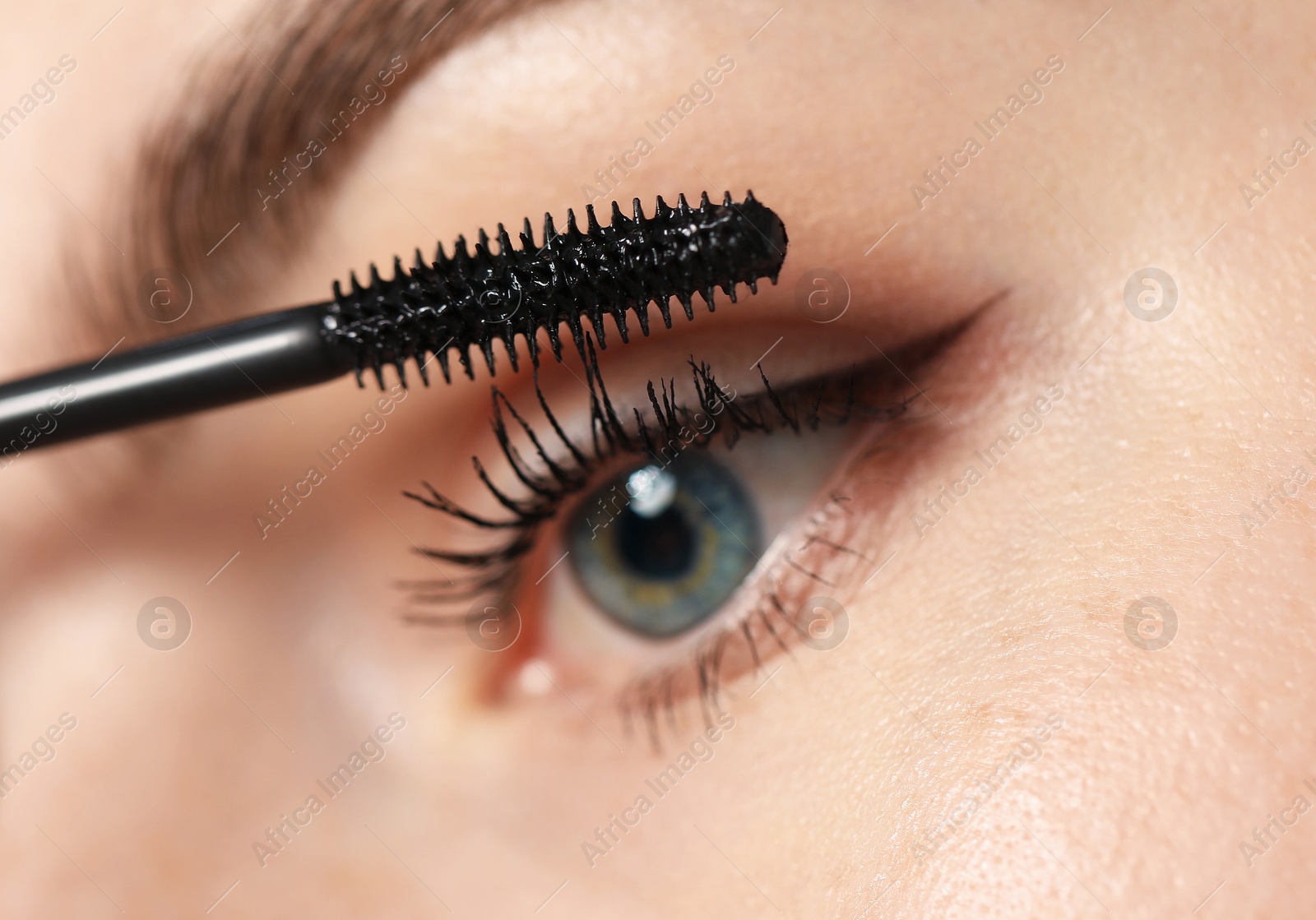 Young woman applying mascara onto her eyelashes, closeup Photo of Young woman applying mascara onto her eyelashes, closeup