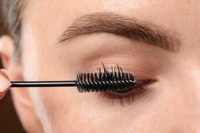 Photo of Young woman applying mascara onto her eyelashes, closeup
