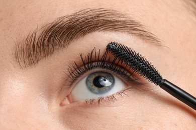 Photo of Young woman applying mascara onto her eyelashes, closeup