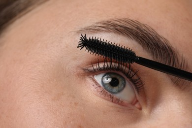 Photo of Young woman applying mascara onto her eyelashes, closeup