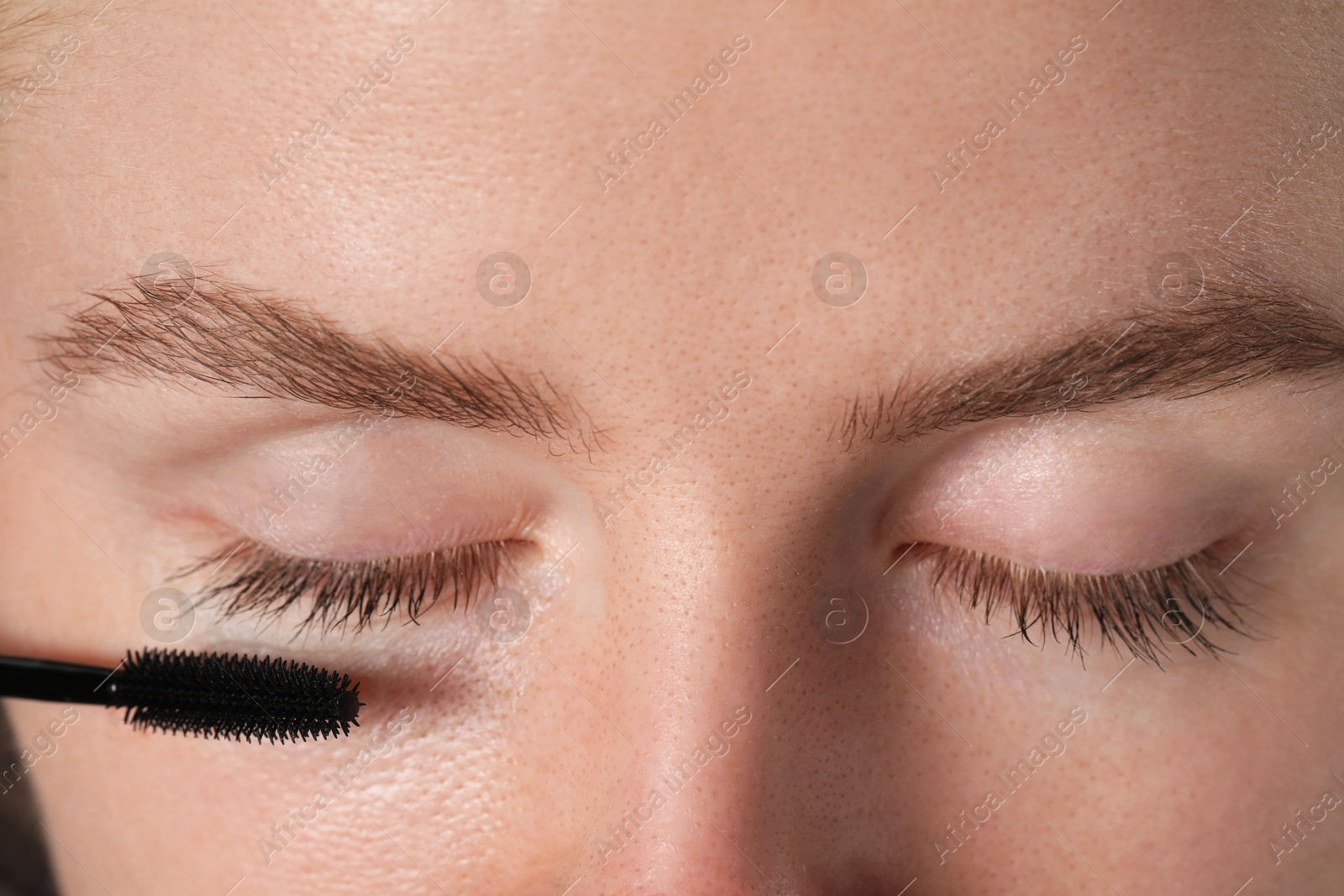 Young woman applying mascara onto her eyelashes, closeup Photo of Young woman applying mascara onto her eyelashes, closeup