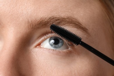 Photo of Young woman applying mascara onto her eyelashes, closeup