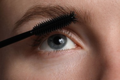 Photo of Young woman applying mascara onto her eyelashes, closeup