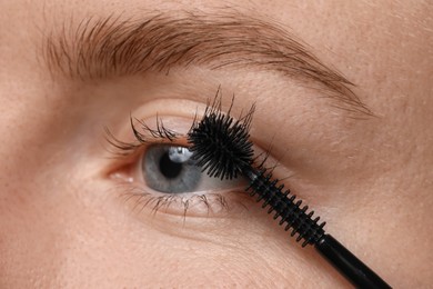 Photo of Young woman applying mascara onto her eyelashes, closeup