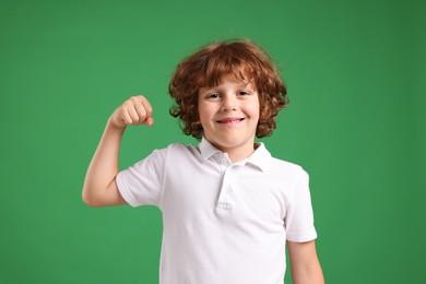 Photo of Strength. Happy little boy showing his biceps on green background