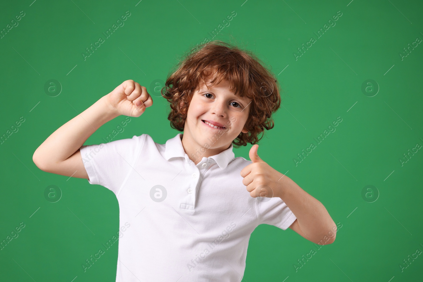 Photo of Strength. Happy little boy showing his biceps and thumbs up on green background