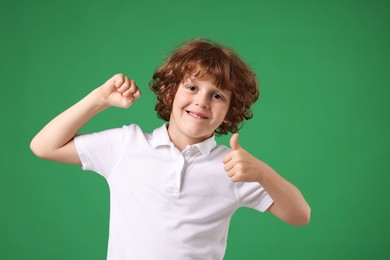 Photo of Strength. Happy little boy showing his biceps and thumbs up on green background