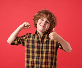 Photo of Strength. Happy little boy showing his biceps and thumbs up on red background