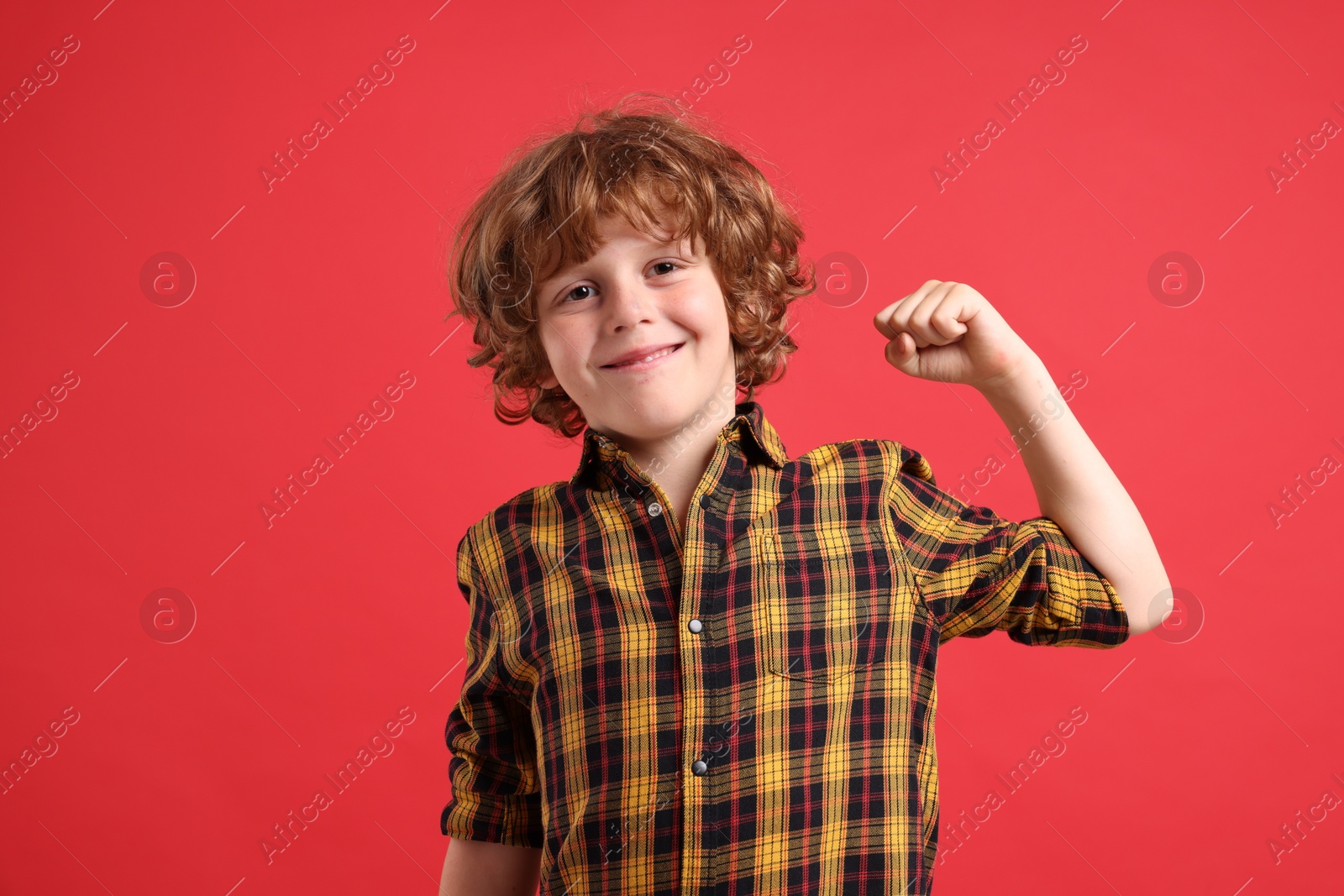 Photo of Strength. Happy little boy showing his biceps on red background