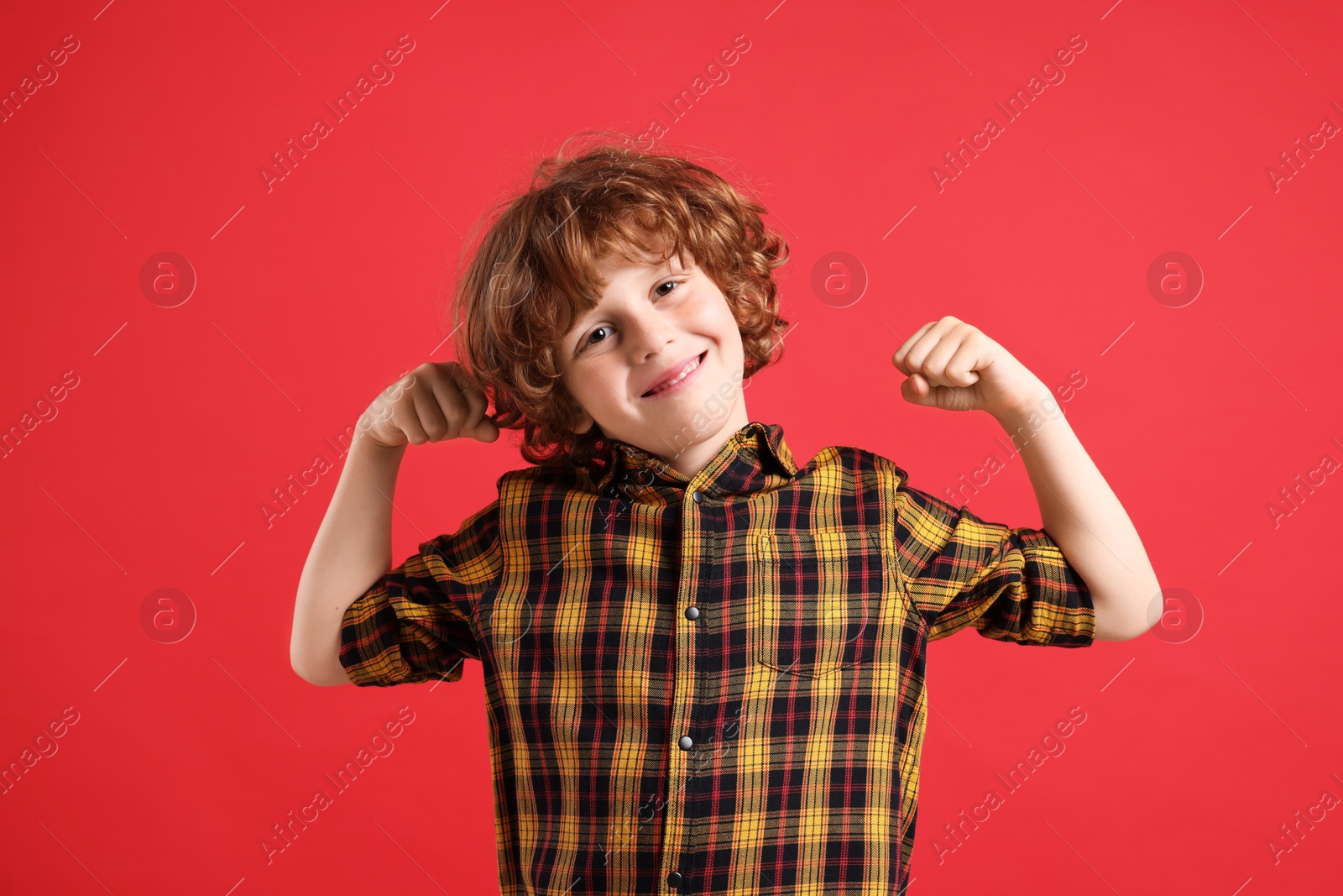 Photo of Strength. Happy little boy showing his biceps on red background