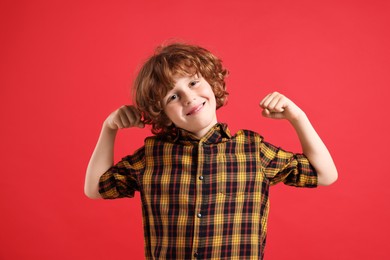 Photo of Strength. Happy little boy showing his biceps on red background