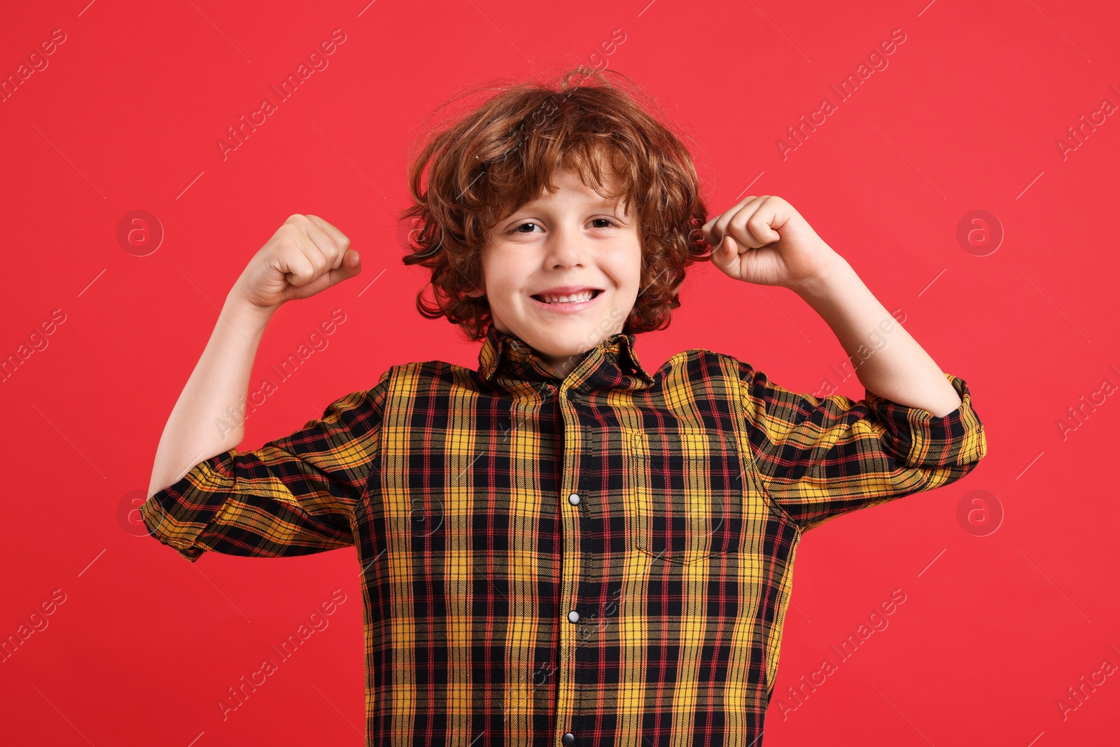 Photo of Strength. Happy little boy showing his biceps on red background