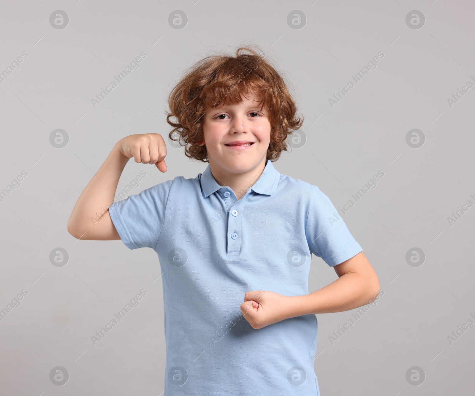 Photo of Strength. Happy little boy showing his biceps on light grey background