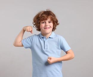 Photo of Strength. Happy little boy showing his biceps on light grey background