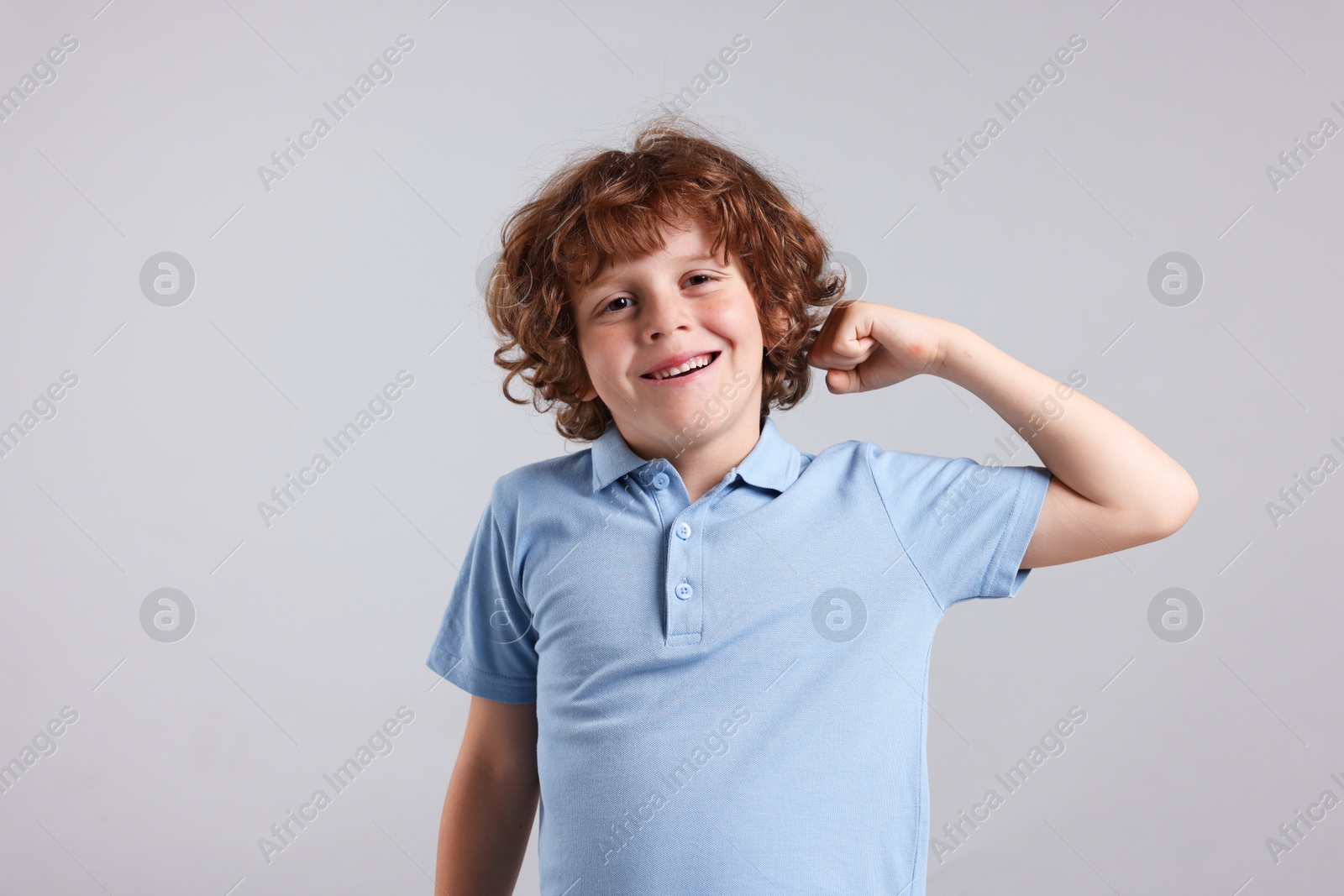 Photo of Strength. Happy little boy showing his biceps on light grey background